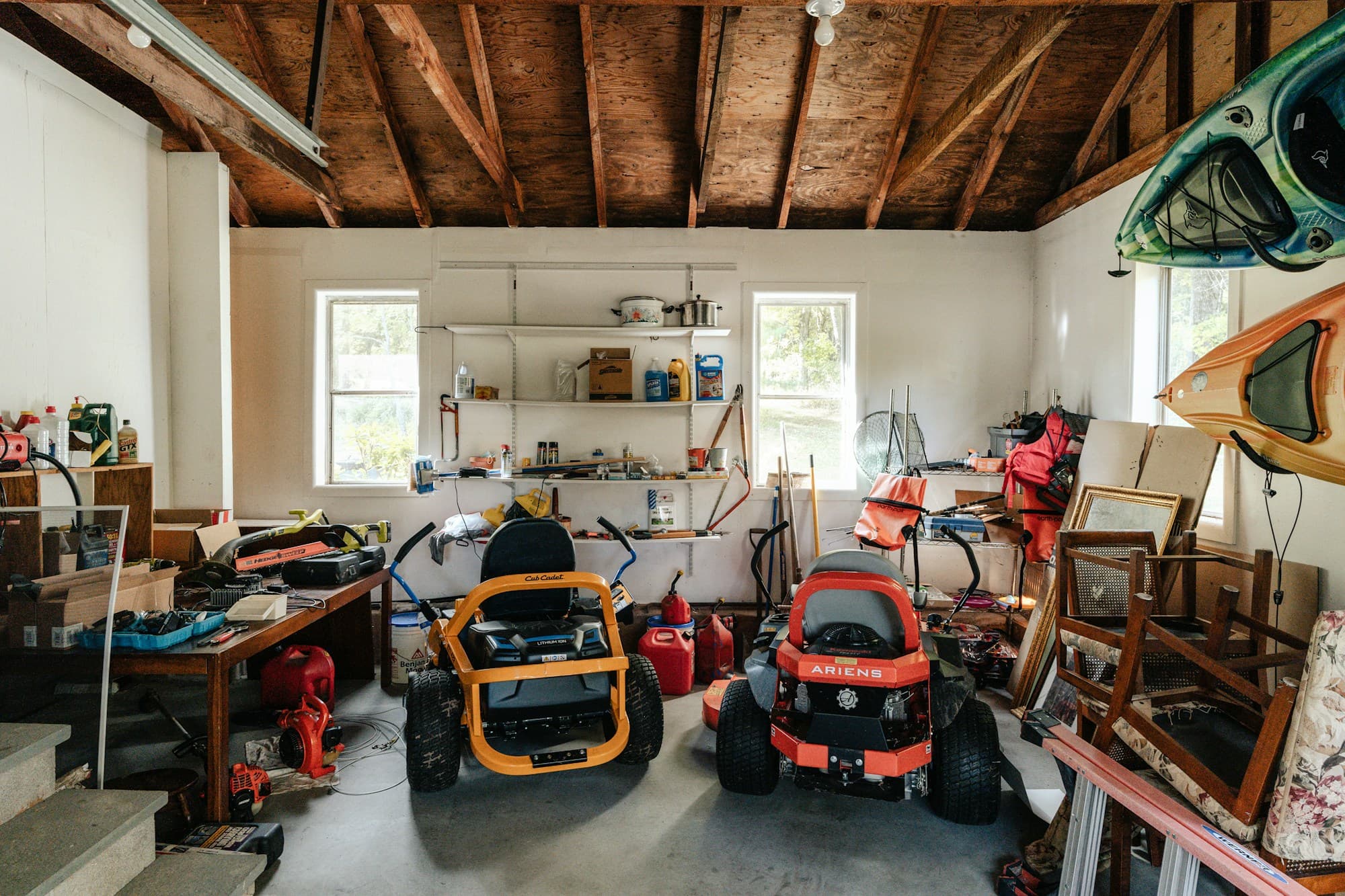 Cluttered home garage filled with lawn equipment, kayaks and stacked belongings
