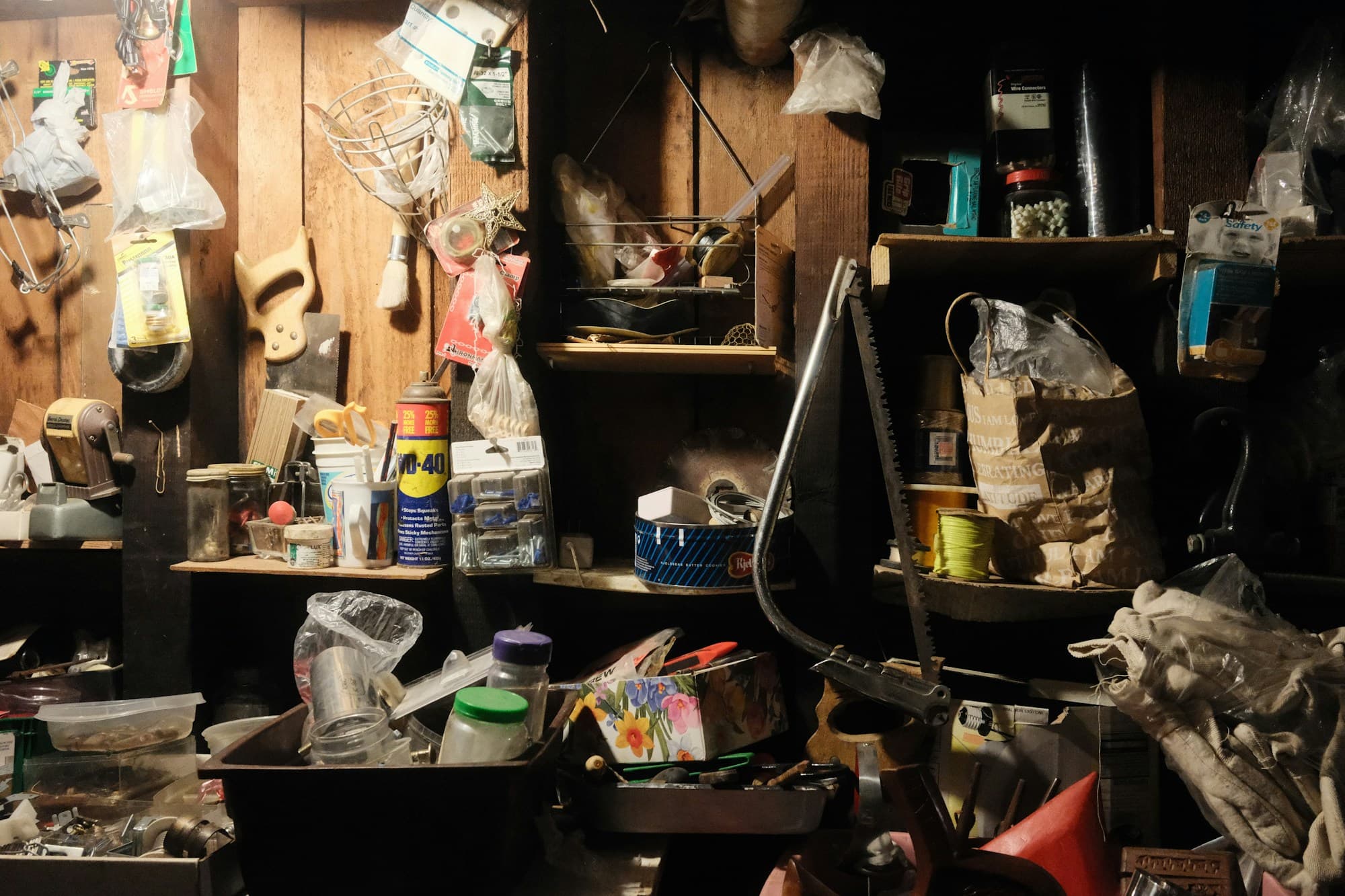 Dim basement workbench crowded with decades of accumulated tools, jars and boxes
